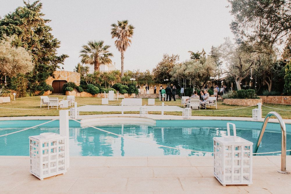 Elegant outdoor wedding venue with a blue swimming pool, white lanterns, and lush garden with palm trees.