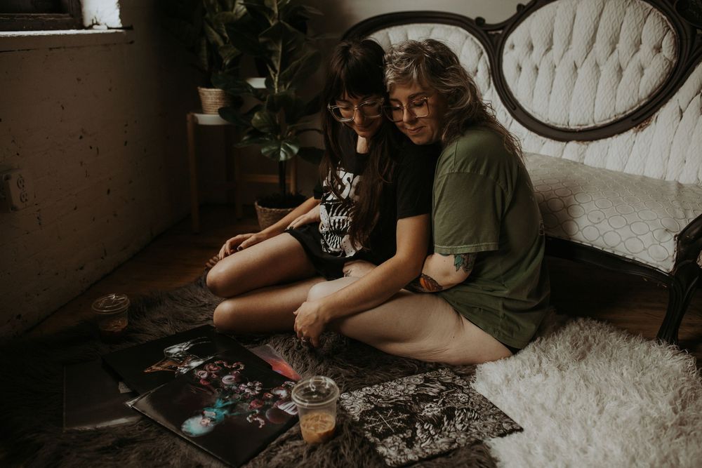 Two women sit on floor looking at photos together in cozy bohemian room.