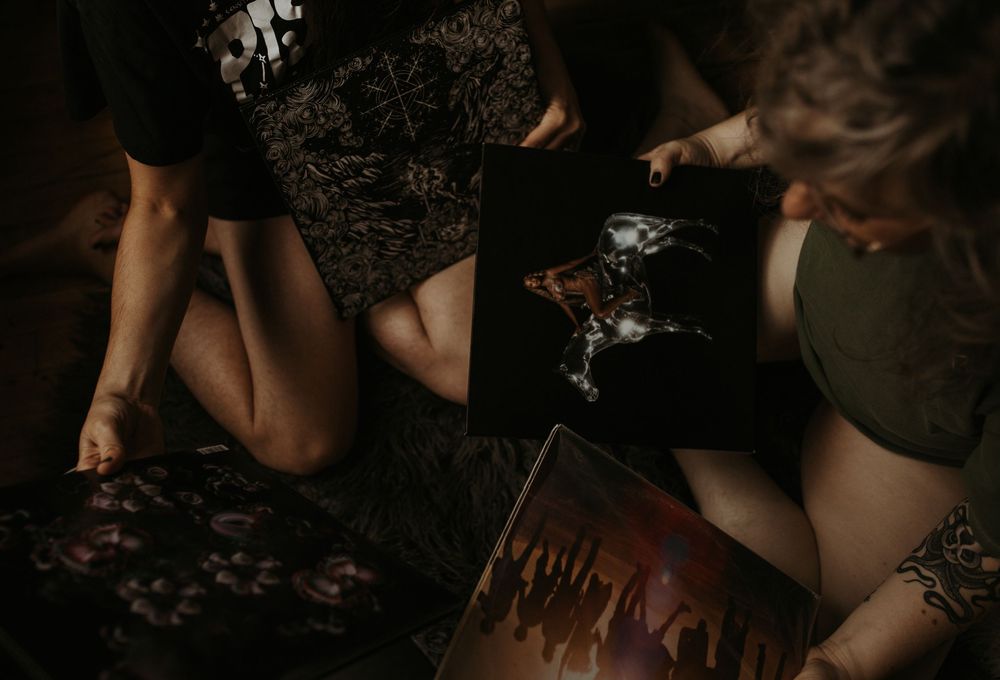Two women sitting on the floor examining vinyl records in a dimly lit room with moody dark tones.