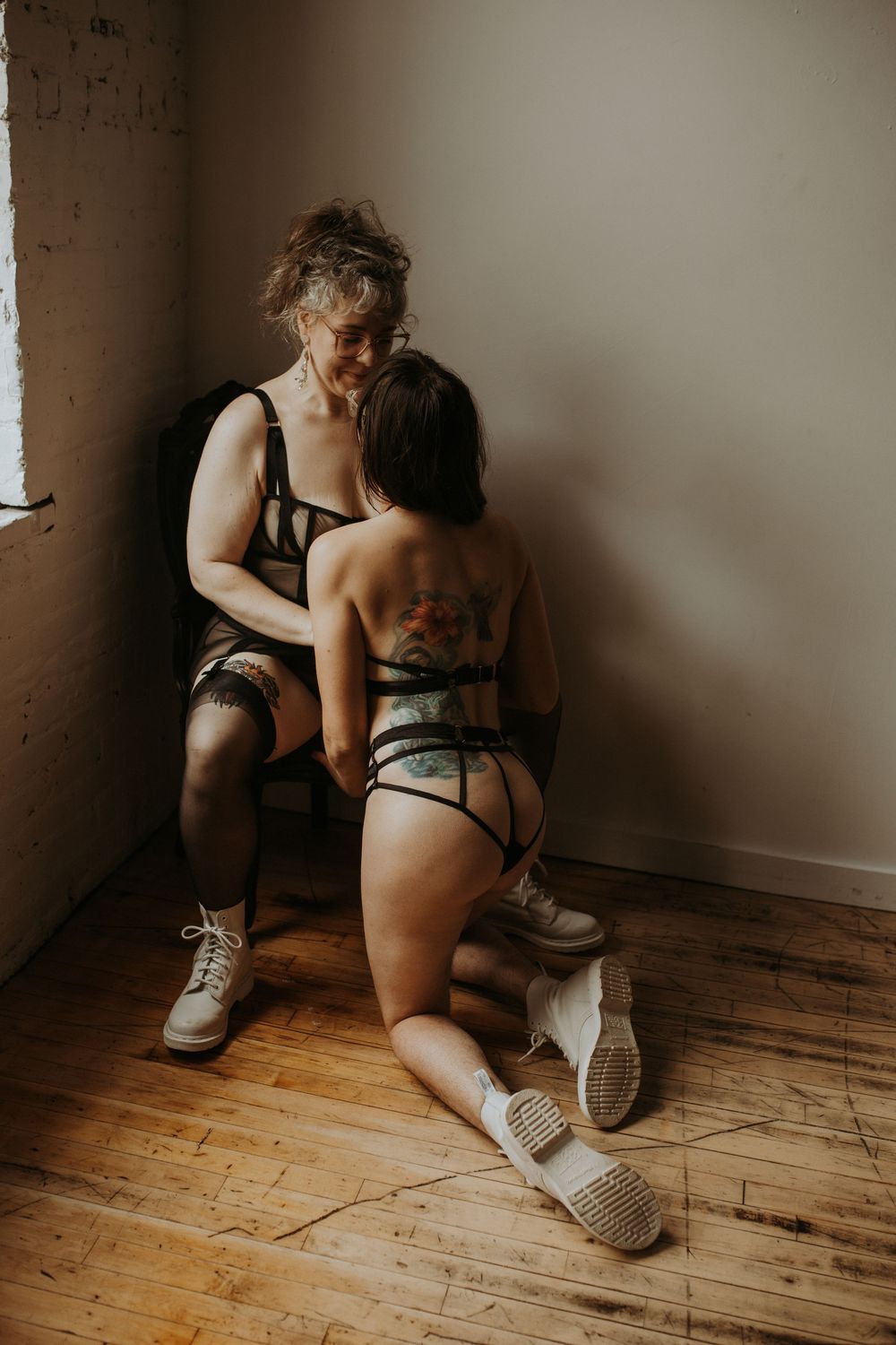 Two women in lingerie sharing intimate moment in minimalist studio space.