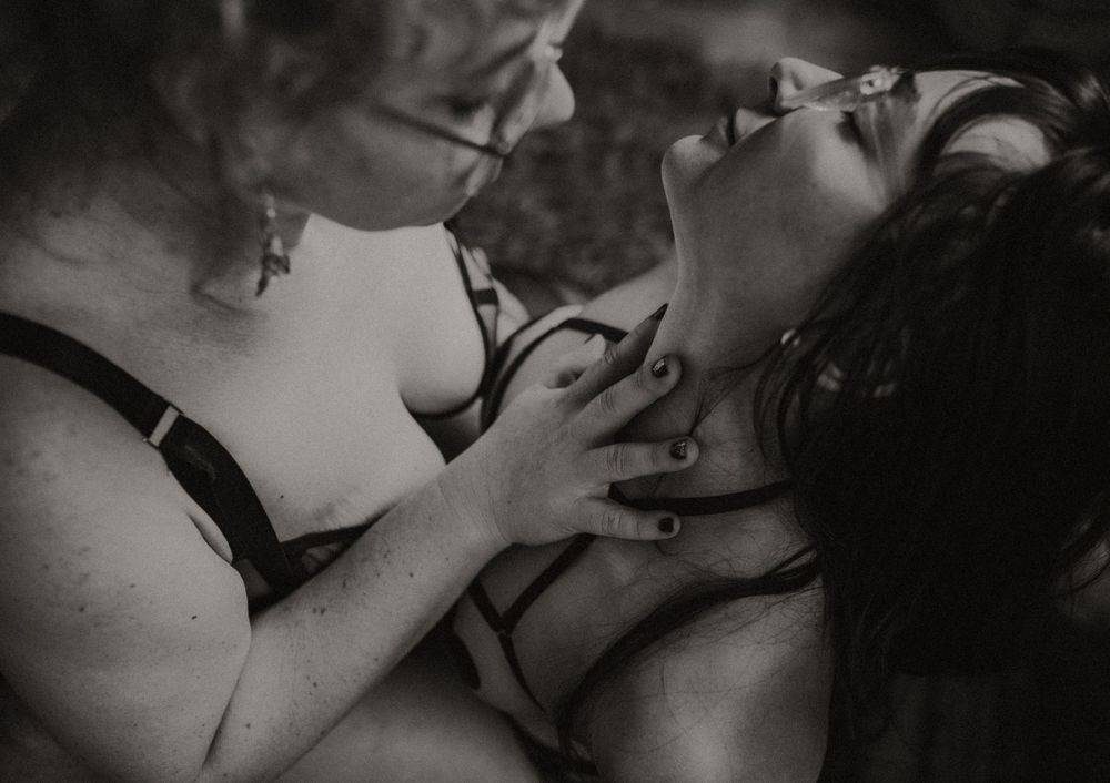 Black and white intimate couple portrait with woman leaning back and man holding her neck in romantic boudoir session.
