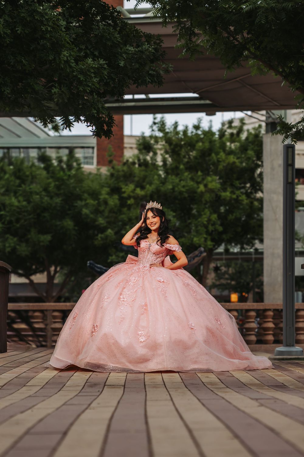 Young woman in a pink ball gown and tiara poses outdoors for her quinceañera celebration.