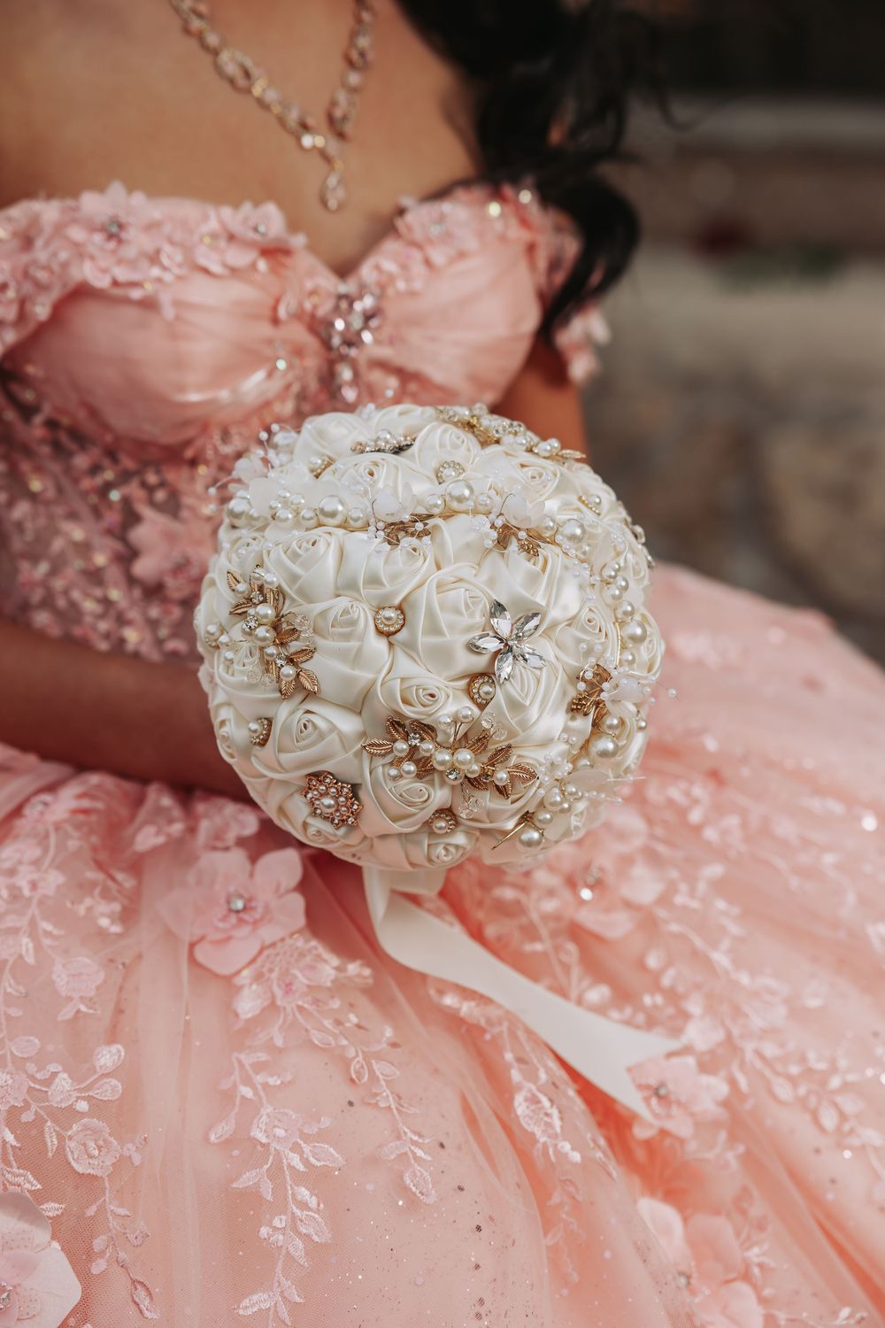 Young woman in pink quinceañera gown holding elegant white and gold brooch bouquet with pearl accents.