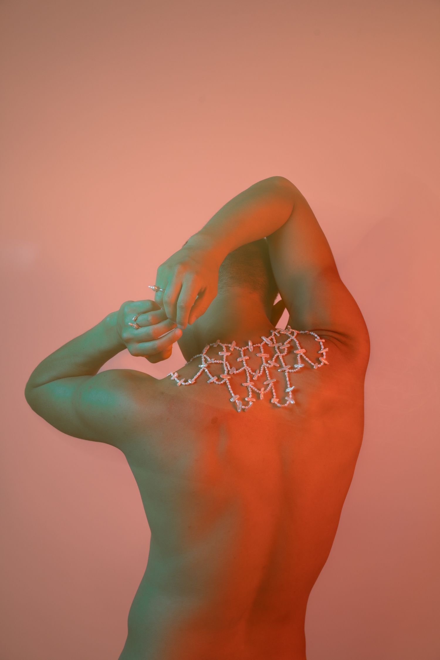 A shirtless person with a molecular structure design on their back poses under red and green studio lighting.