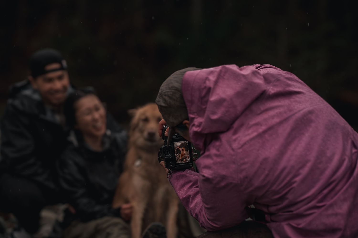 A woman photographs a young Asian couple and their dog while it rains.