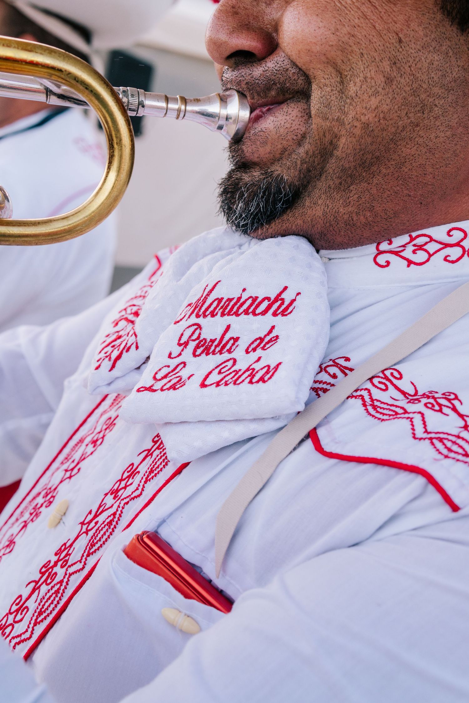 Mariachi Perla de Los Cabos musician playing trumpet in traditional white and red embroidered uniform.