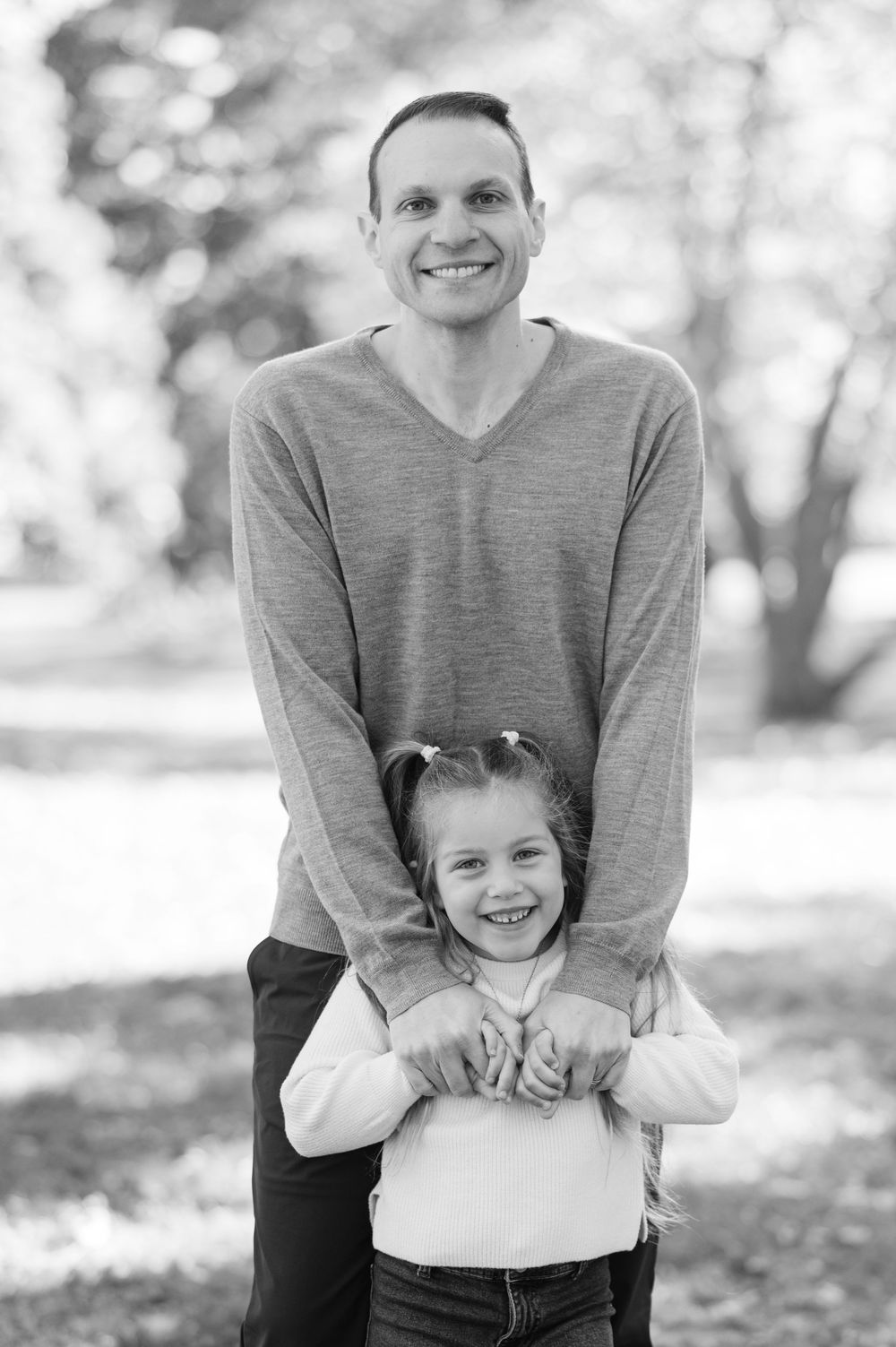 Black and white photo of a smiling man and young girl posing together outdoors in a park setting.