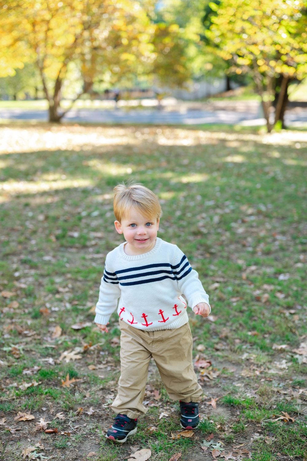 Toddler boy in nautical anchor sweater and khaki pants smiling in autumn park.
