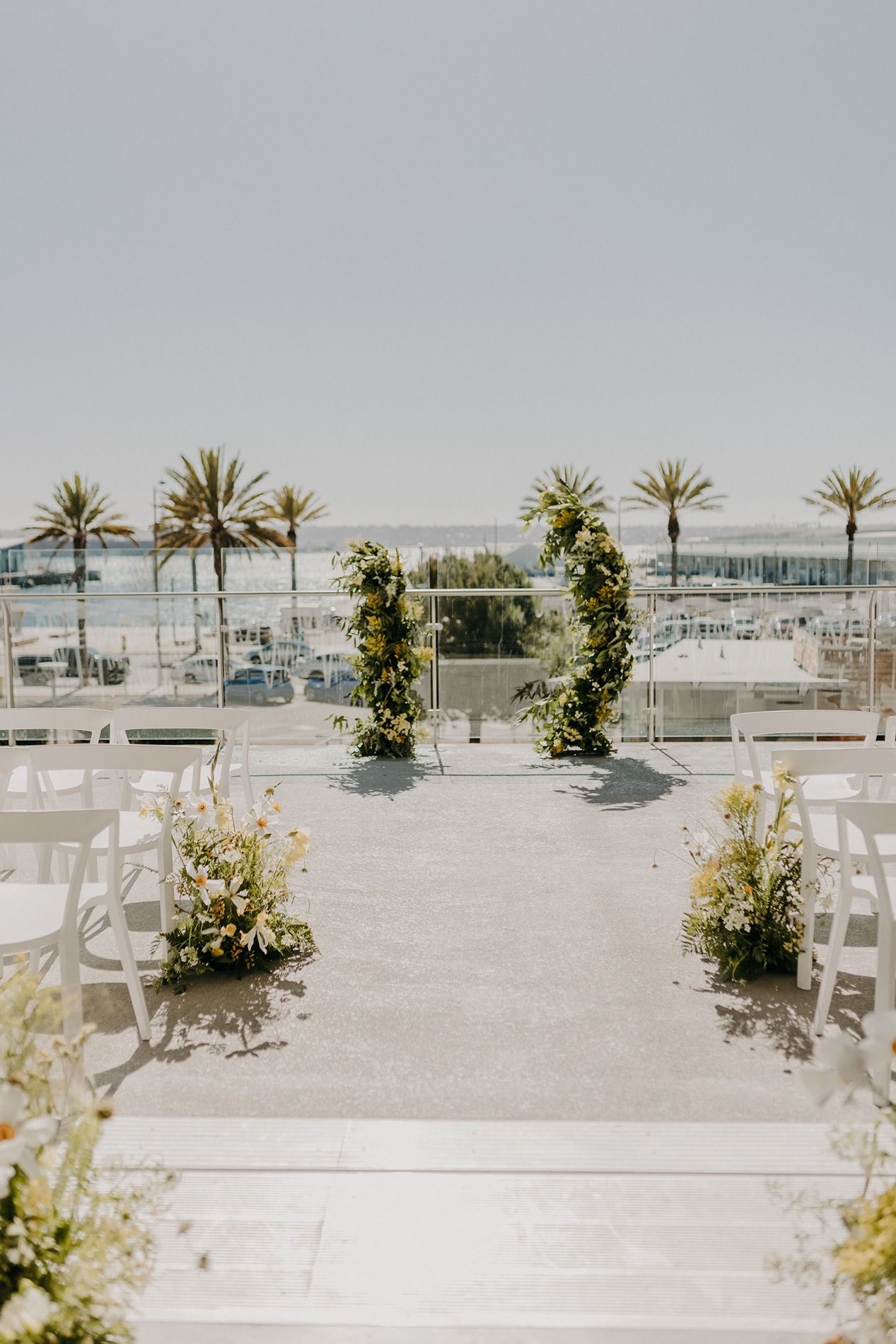 Outdoor rooftop wedding ceremony with floral arch, white chairs, and palm trees under a clear sky at The Lane.