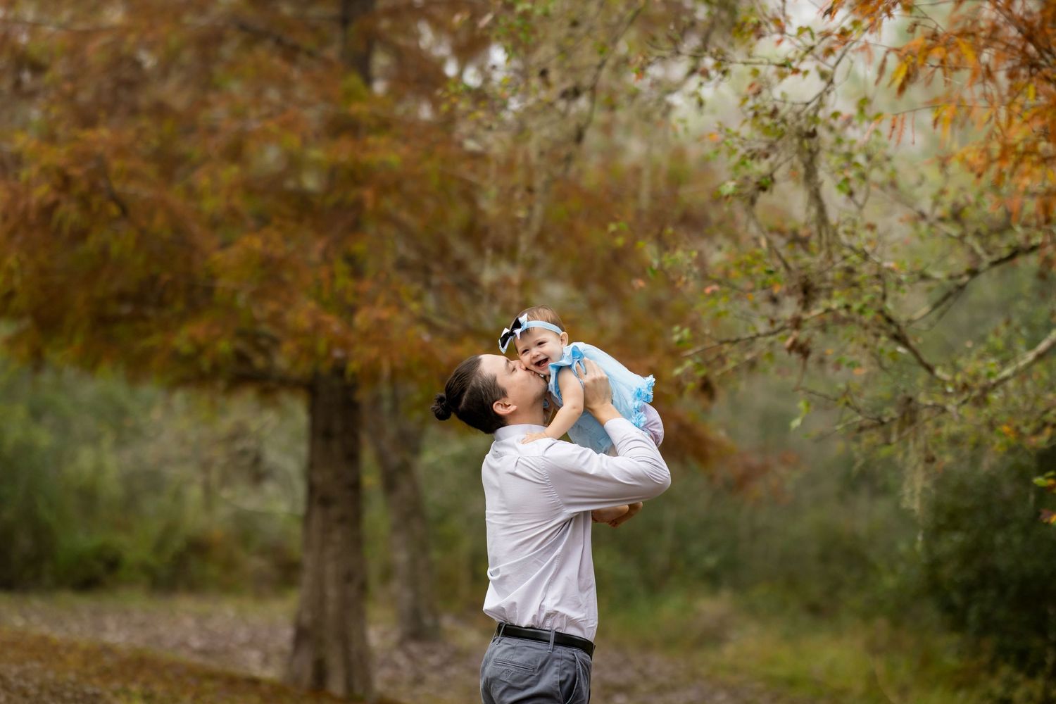 A parent joyfully lifts a baby in an autumn park surrounded by colorful trees.
