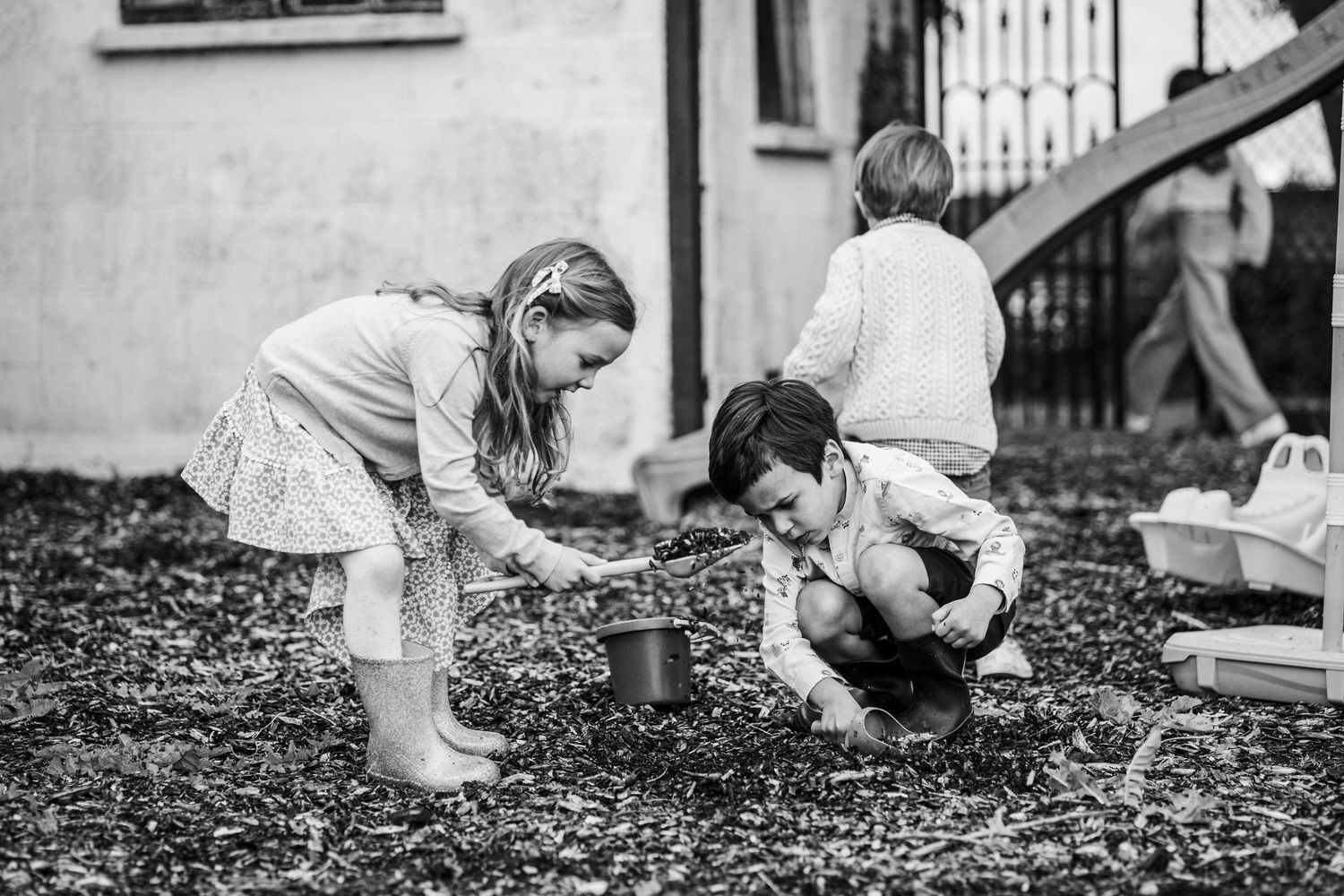 Black and white photo of two young children playing in a garden, digging in the dirt near a small pot.