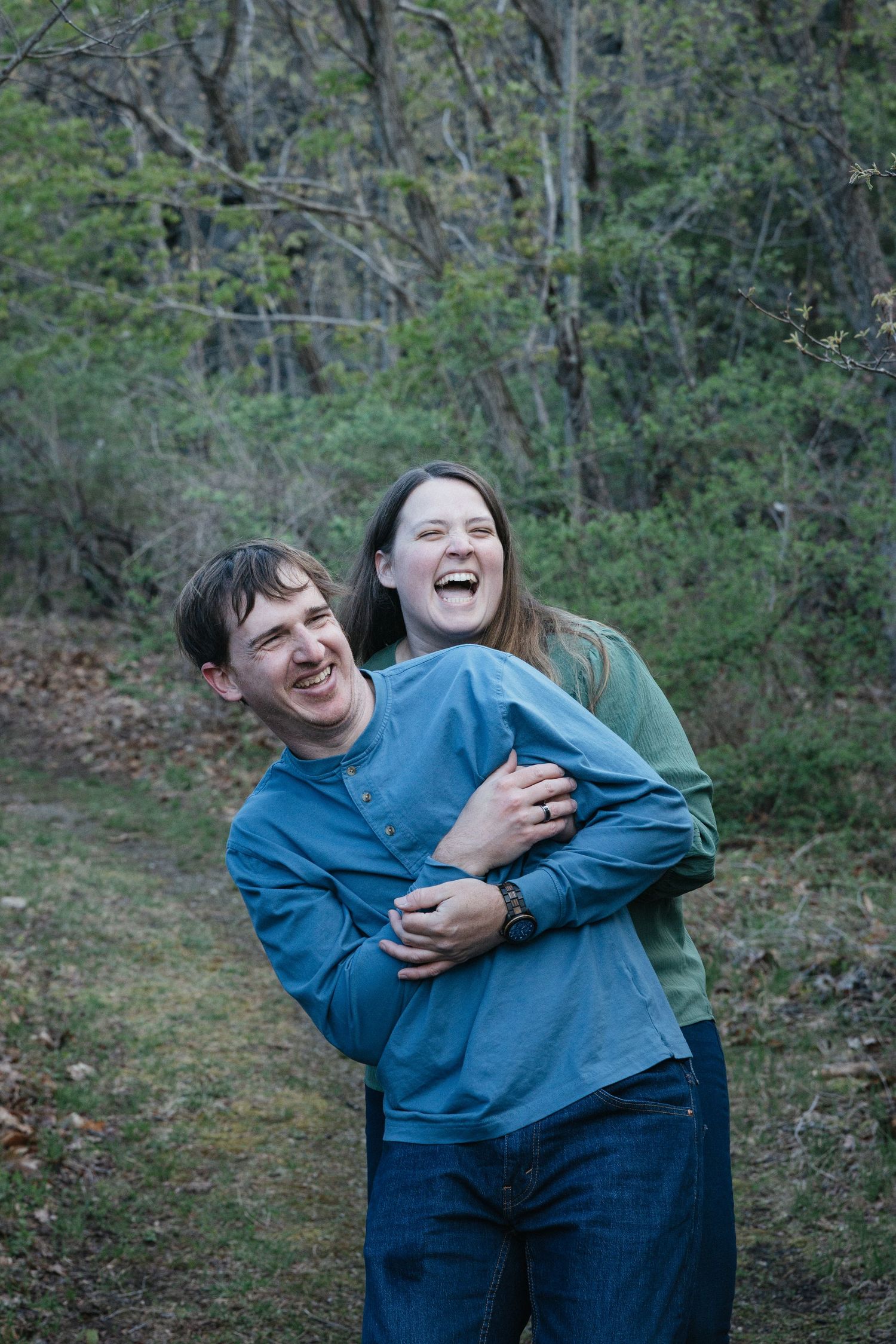 A happy young couple holds hands while walking through a grassy hilltop with scenic mountain views under a cloudy sky.