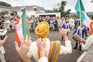 Colorful Indian wedding celebration with guests waving flags and hands outdoors.
