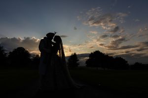 Silhouette of a couple sharing a romantic kiss at sunset with dramatic clouds and trees in the background.