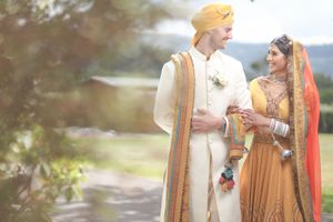 Couple in traditional Indian wedding attire smiling outdoors.