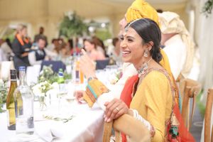 Smiling bride in yellow Indian bridal attire at wedding reception table.