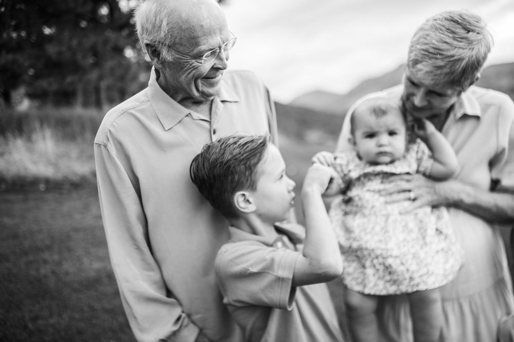 Grandparents smiling and bonding with young grandchildren outdoors in a black and white family portrait.