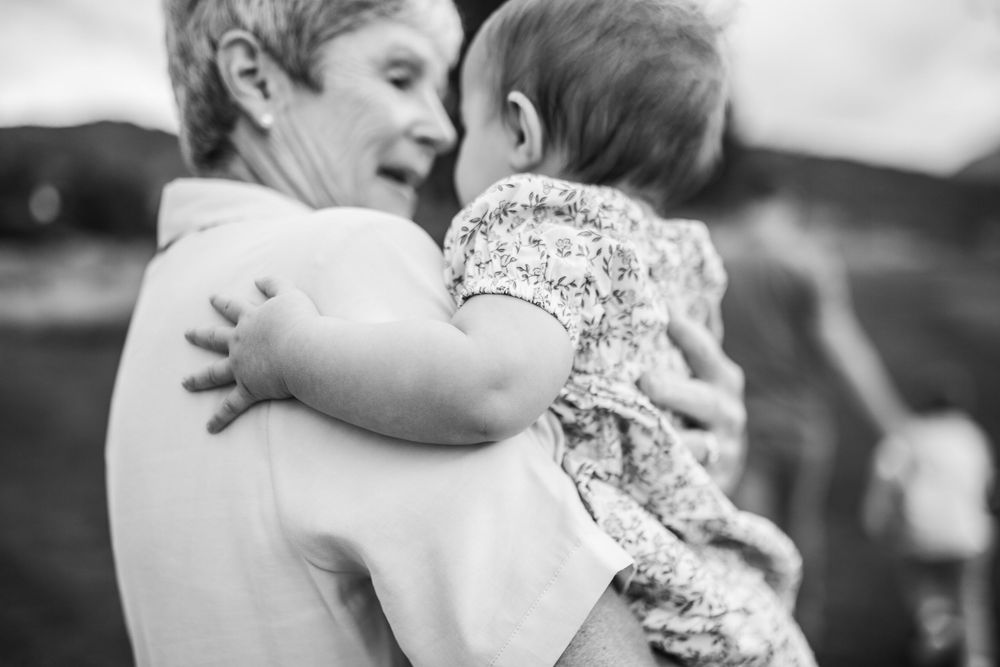 Grandmother lovingly holding and smiling at baby in black and white outdoor portrait.