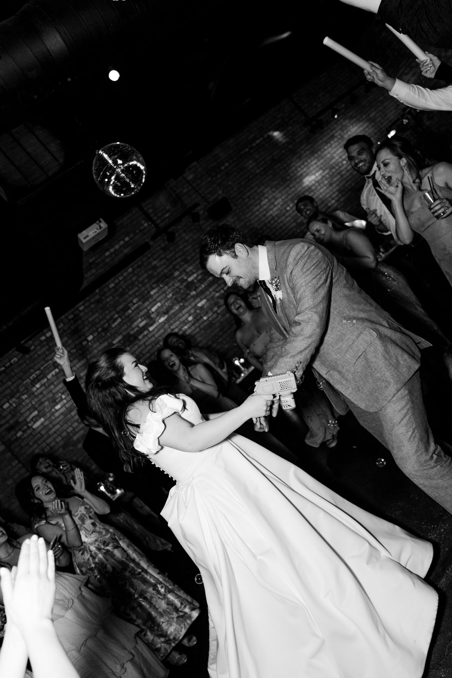 Black and white photo of bride and groom sharing first dance at wedding reception with guests watching.