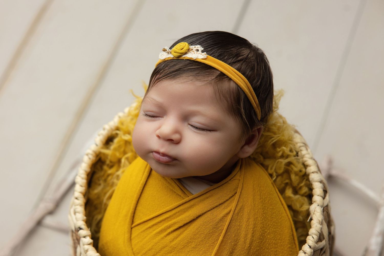 Newborn baby resting chin on hands inside a teal bucket with soft blanket, studio photography.