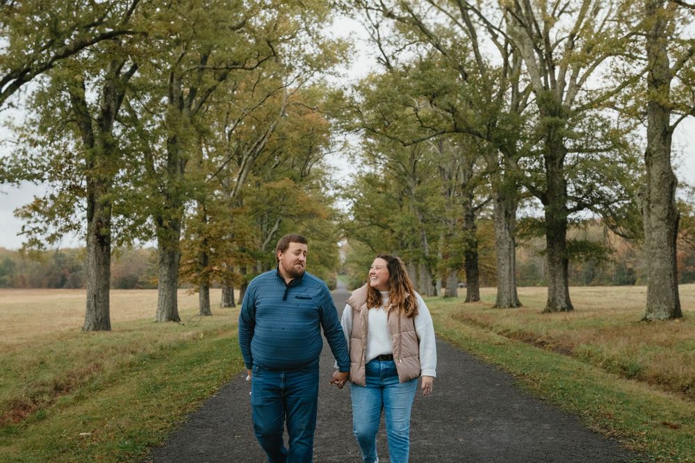 Couple holding hands walking down a tree-lined path in a park during autumn.