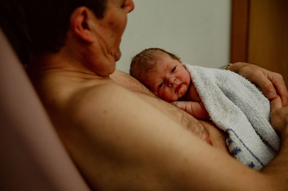 Newborn baby wrapped in a white towel resting on a parent's bare chest after birth.