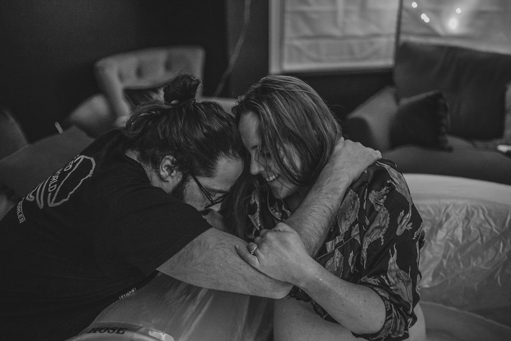 Black and white photo of two women sharing an emotional embrace, leaning foreheads together in a tender moment.