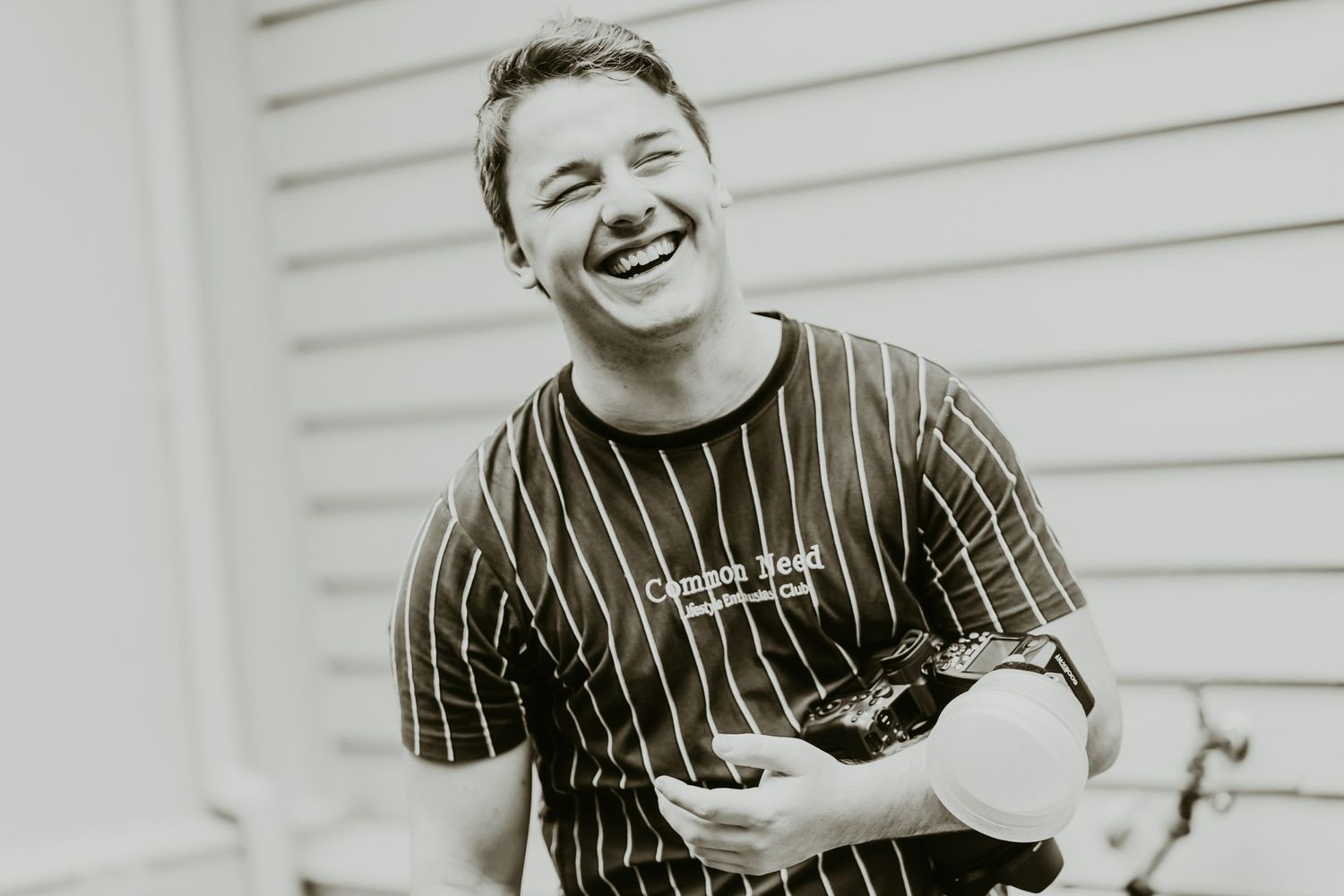 Young person laughing joyfully outdoors, wearing a striped t-shirt, holding an object in a black and white photo.