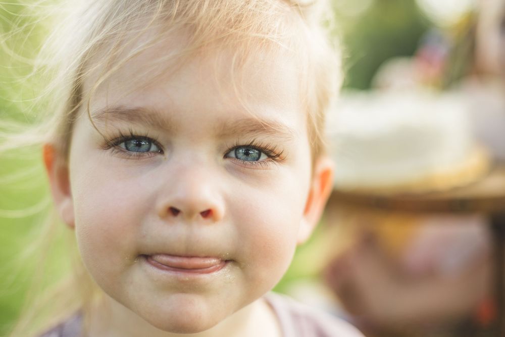 Close-up portrait of a young blonde child with blue eyes smiling outdoors in natural light.
