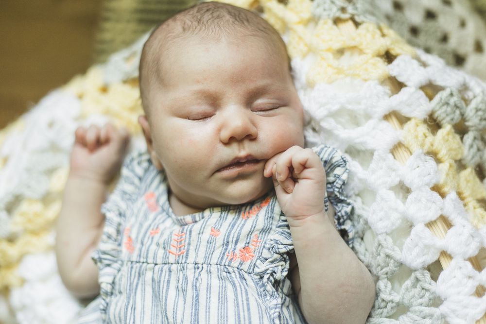 Peaceful newborn baby sleeping on a crocheted blanket wearing a striped outfit with tiny floral details.