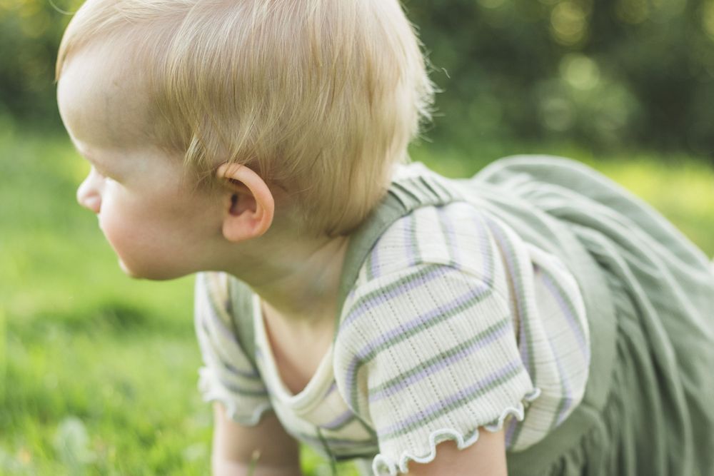 Blond baby crawling on green grass outdoors in summer, wearing a striped romper.