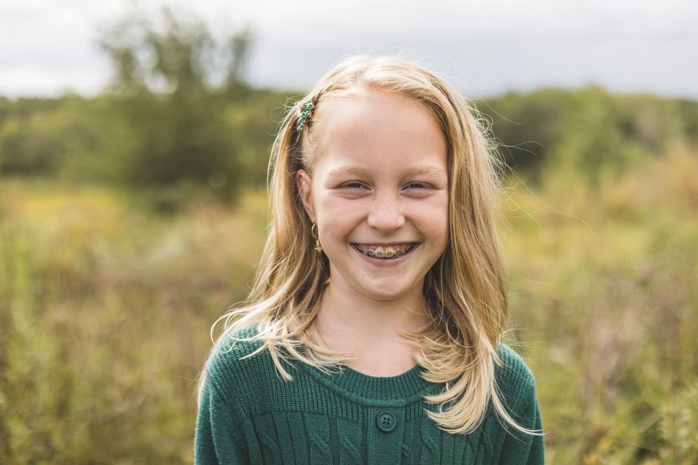 Smiling blonde girl in green sweater outdoors in a field, portrait photo.