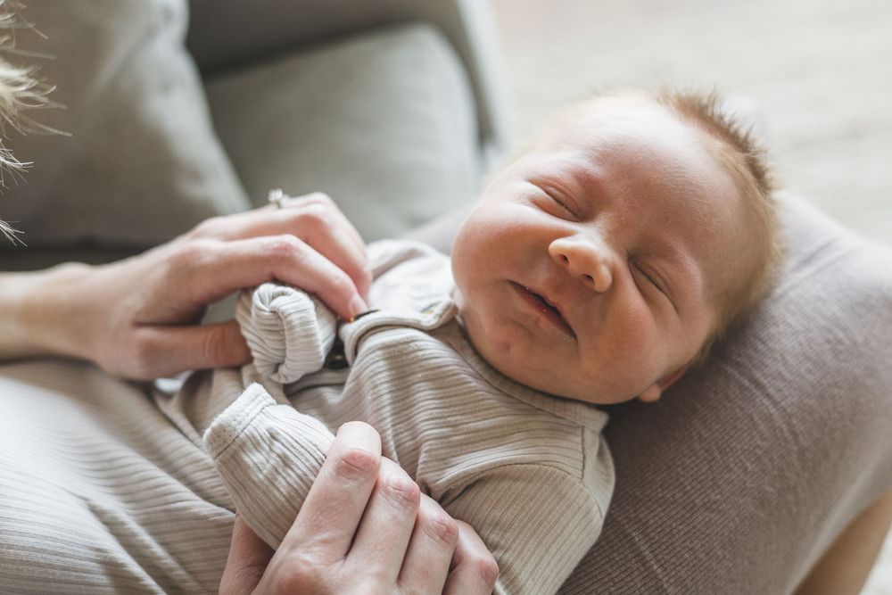 Newborn baby sleeping peacefully in parent's arms wearing a striped onesie.