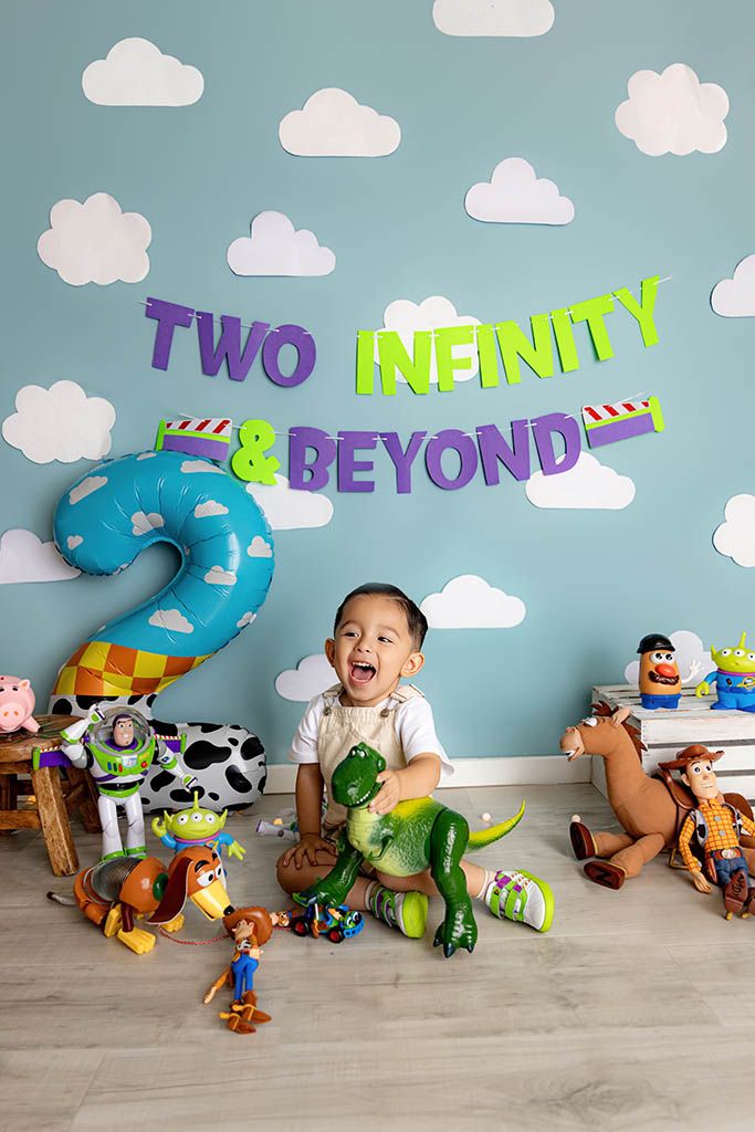 Toddler boy celebrates 2nd birthday with Toy Story theme, surrounded by character toys under Two Infinity and Beyond banner.