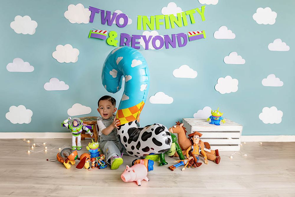 Toddler boy sits with Toy Story toys and a number 2 balloon under a Two Infinity and Beyond birthday banner.