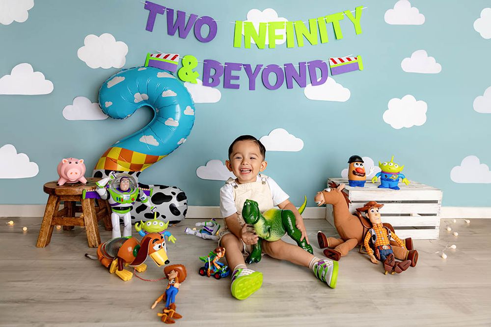 Toddler boy celebrates 2nd birthday with Toy Story themed party, surrounded by character toys and Two Infinity Beyond banner.