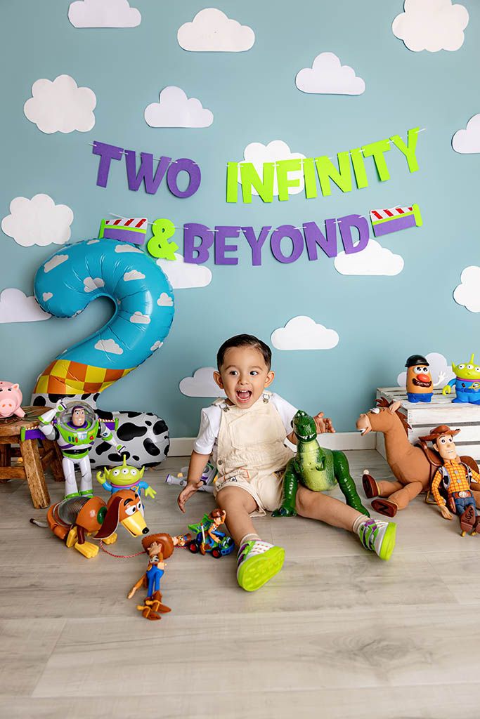 Toddler boy celebrates 2nd birthday with Toy Story theme, surrounded by character toys and Two Infinity and Beyond banner.
