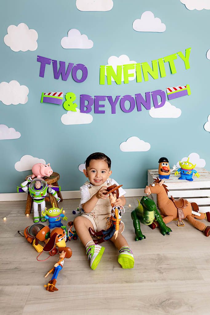 Two-year-old boy sits with Toy Story character toys under a Two Infinity and Beyond banner at his birthday photo shoot.