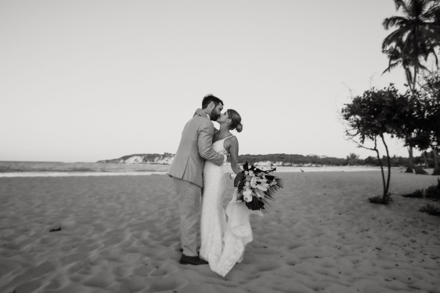 A series of beach wedding photos in black and white showing romantic moments between a couple on a tropical shoreline.