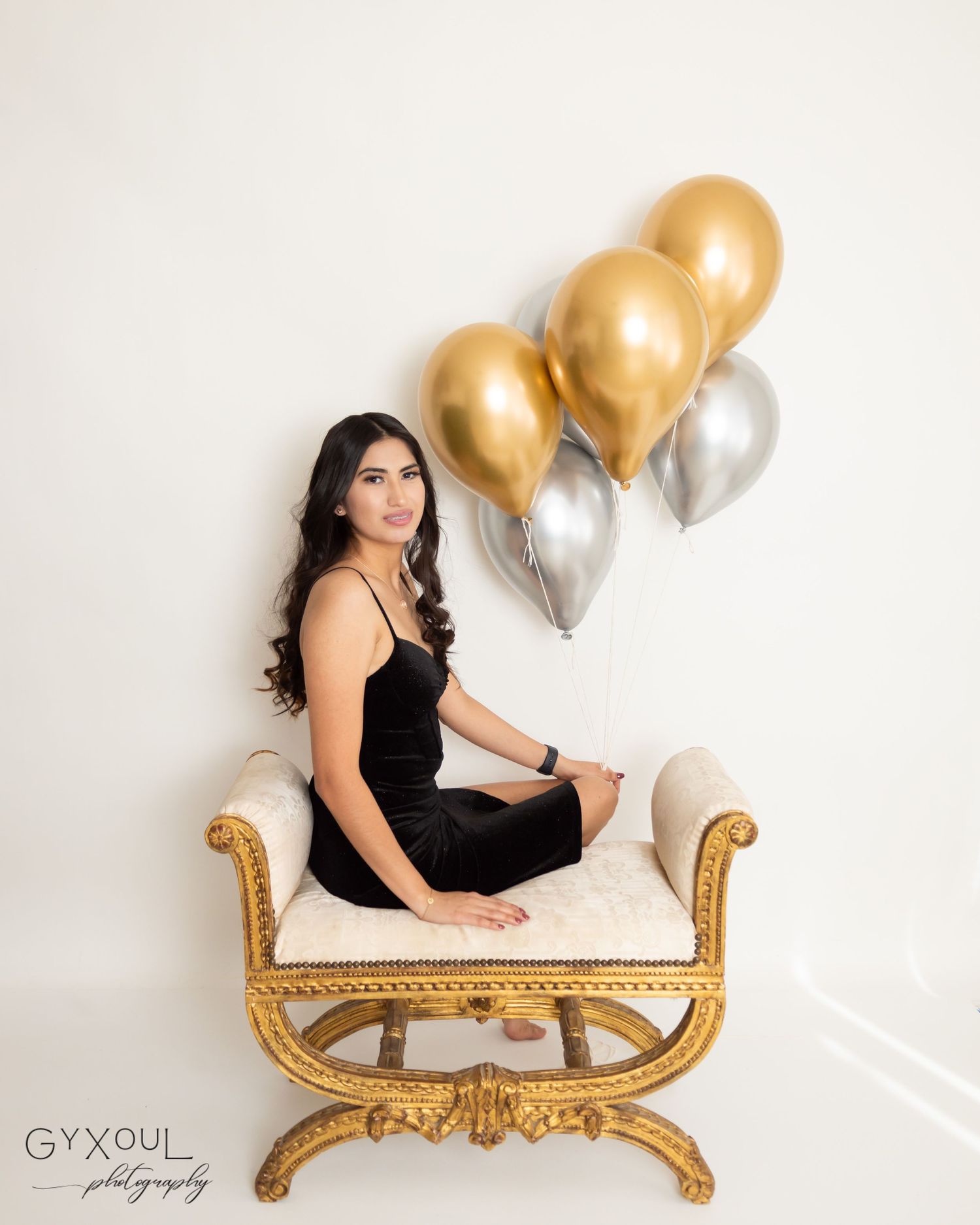 Glamorous portrait session with gold and silver balloons on an ornate white chair.
