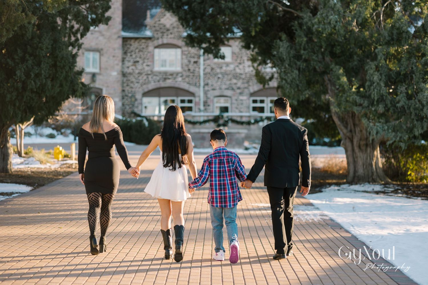 Family holding hands while walking away on brick pathway near stone building.