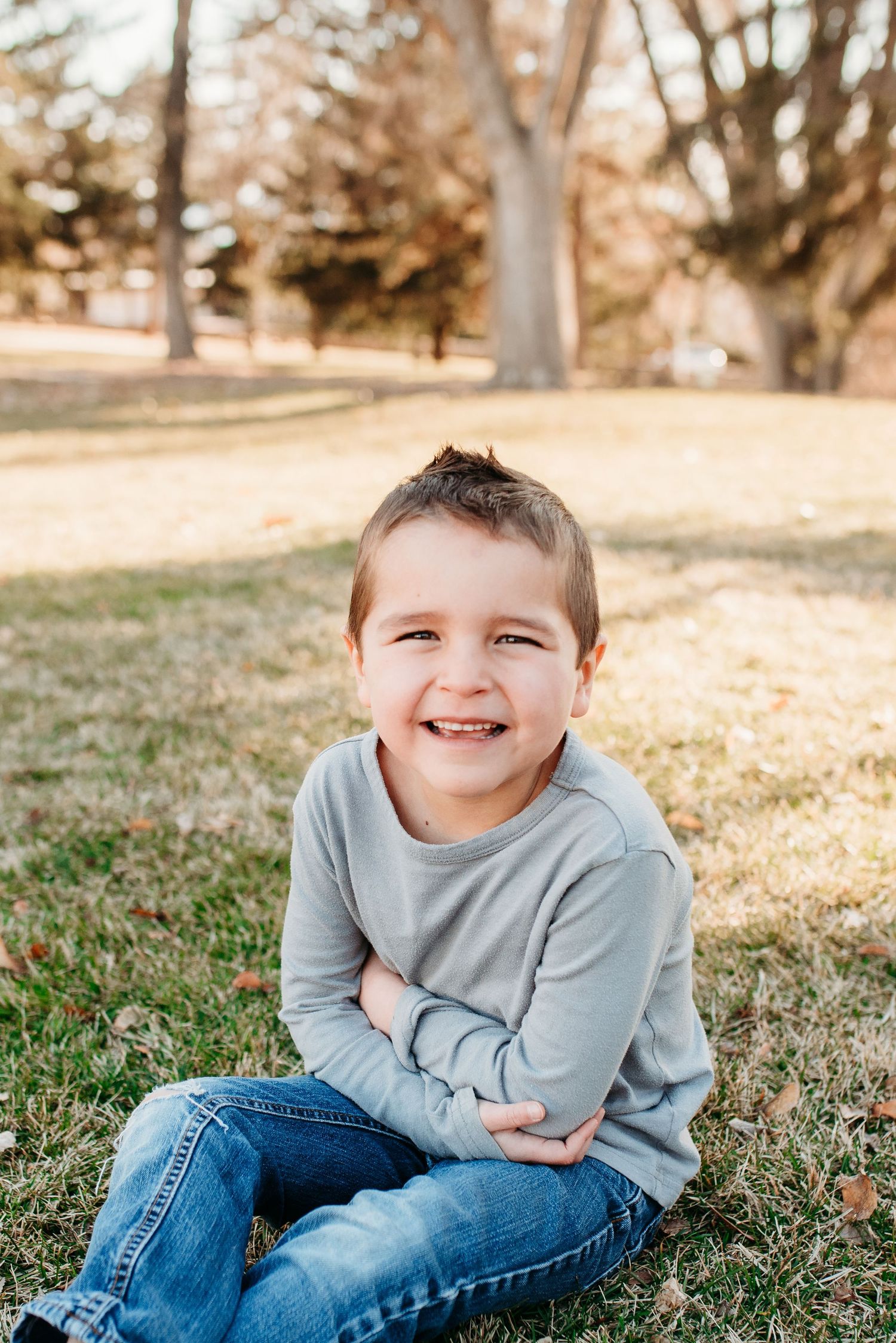 Young child sitting on grass wearing blue sweater and jeans during an autumn outdoor photoshoot.