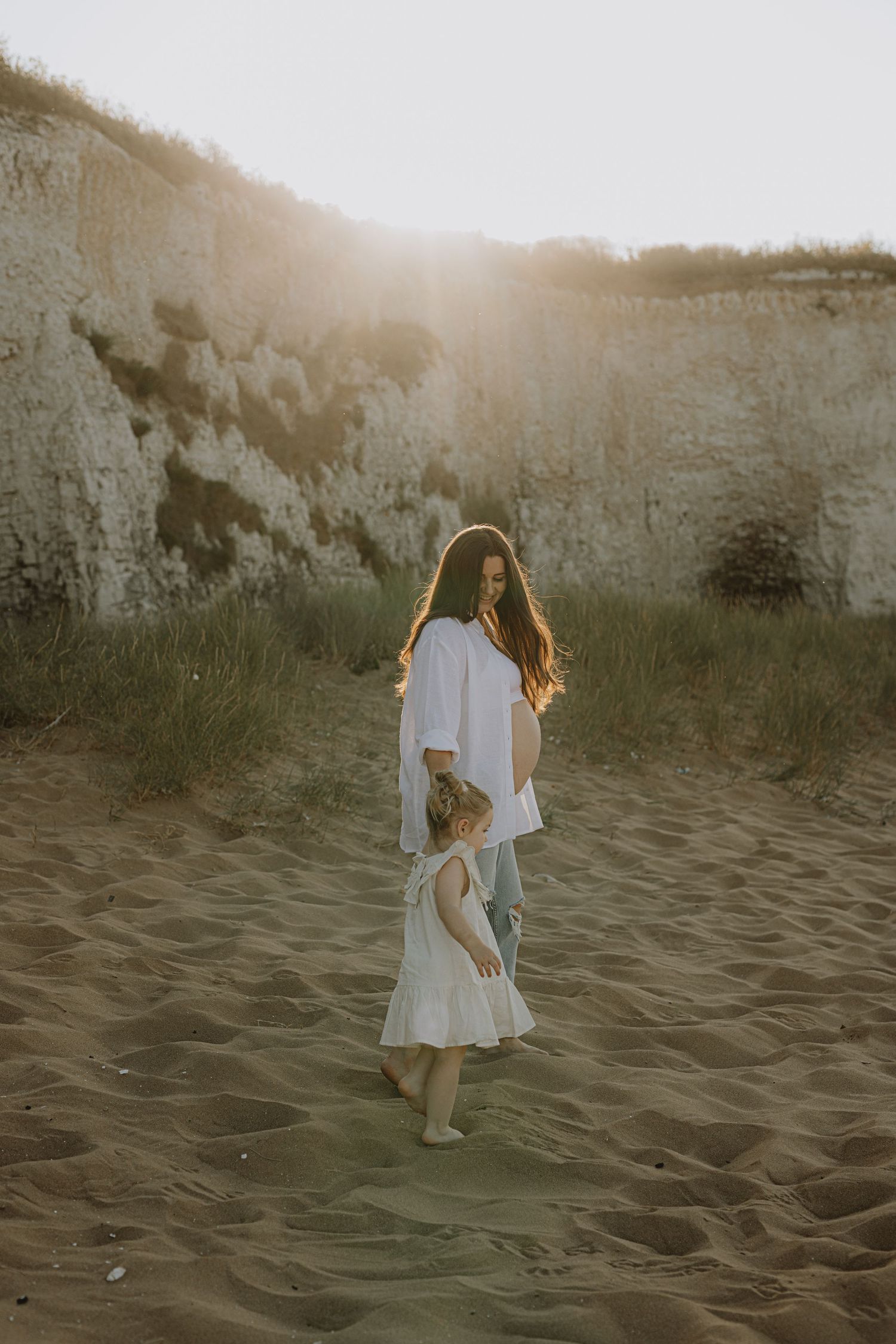 Two figures in white clothing dance together on sandy dunes during golden hour.