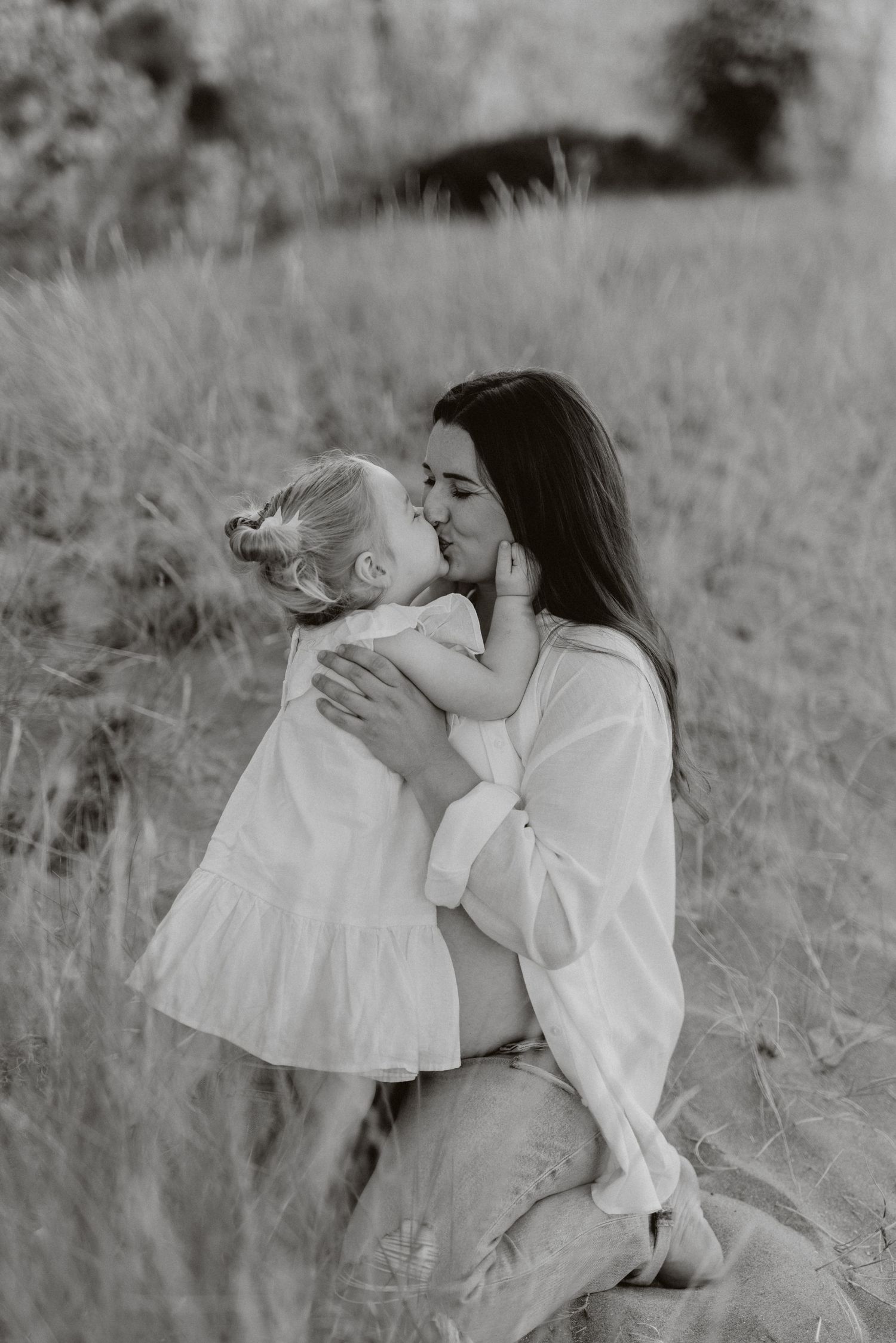 Black and white portrait capturing an intimate family moment on sandy terrain.