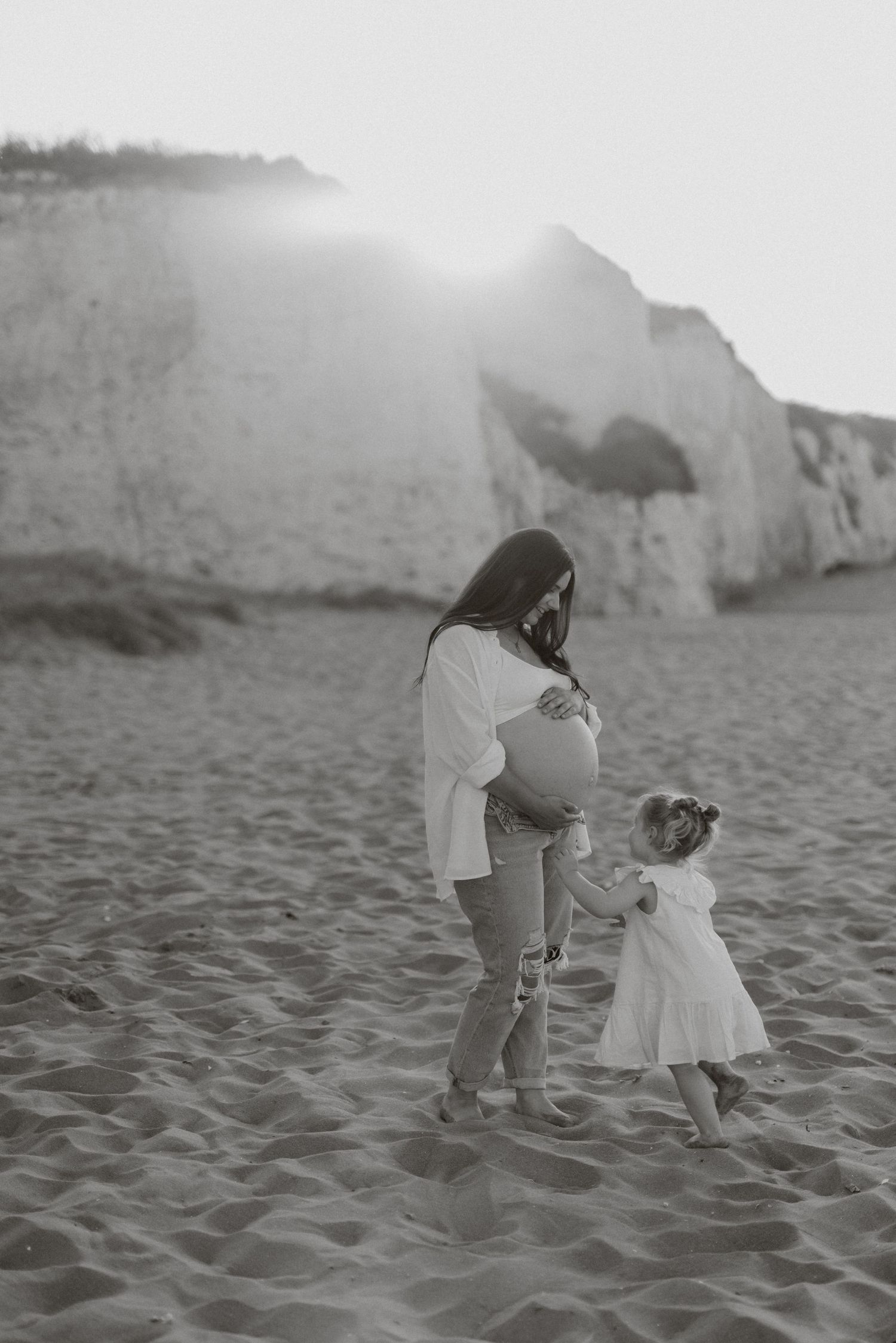 Black and white photo of two people playing in the sand near coastal cliffs.