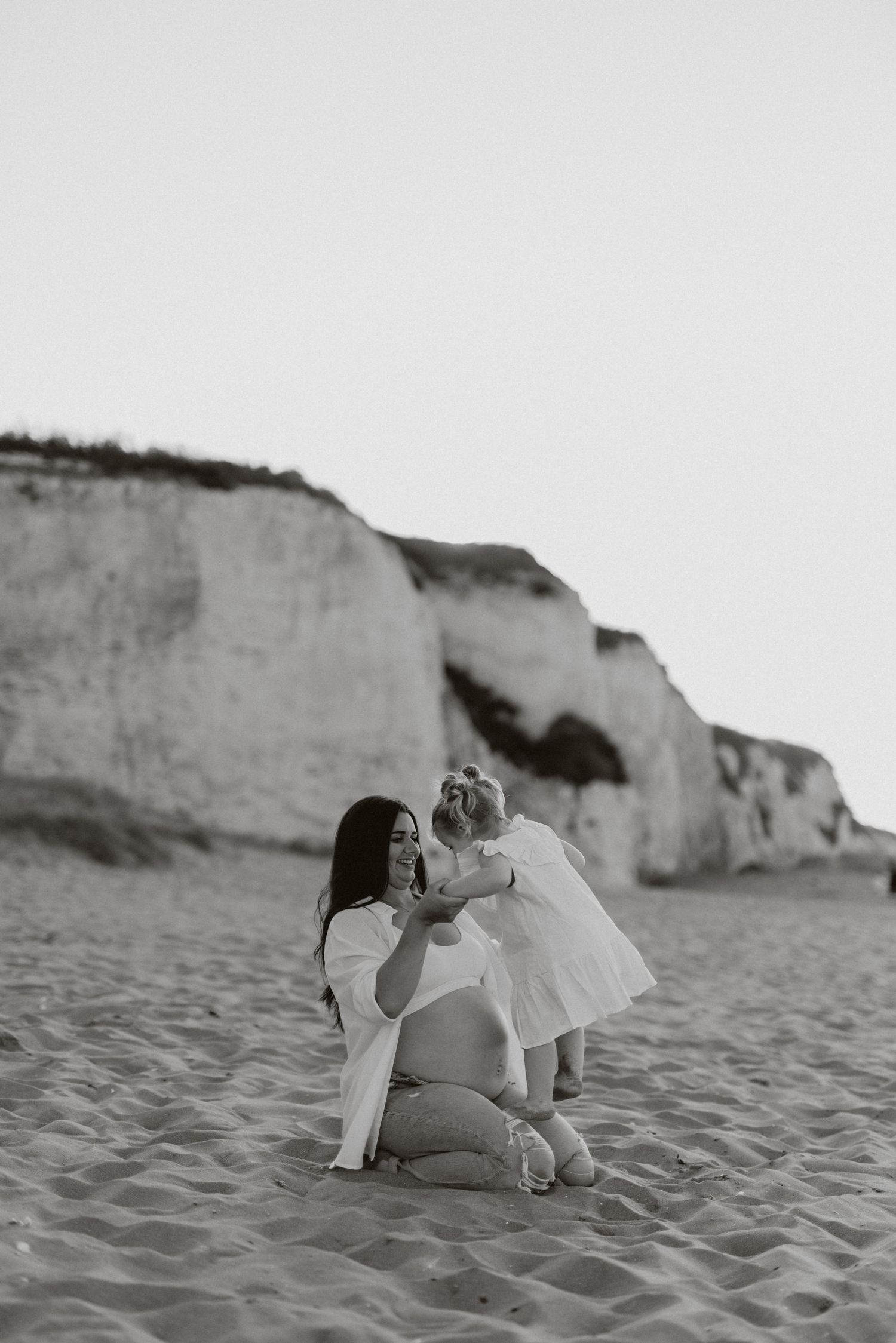 Black and white beach scene with family members sharing a quiet moment near cliffs.
