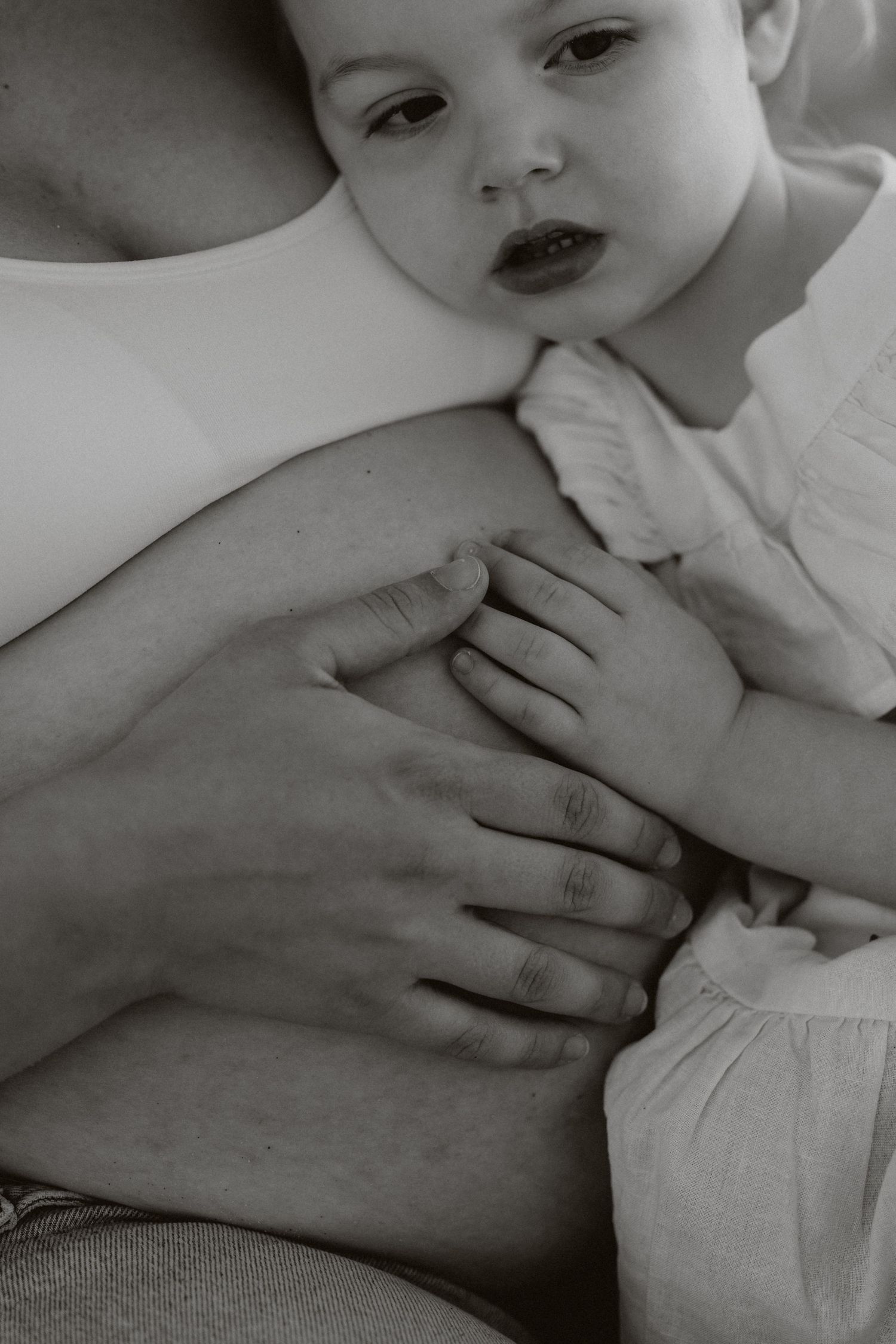 Black and white close-up of a gentle hand caressing a baby in soft lighting.
