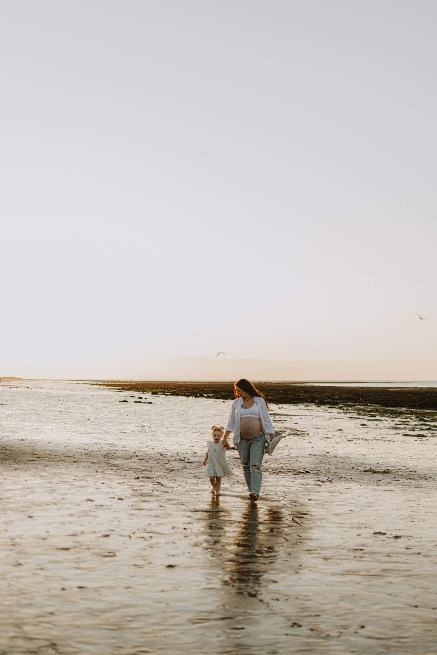 Two people walking together on a wet beach during golden hour.