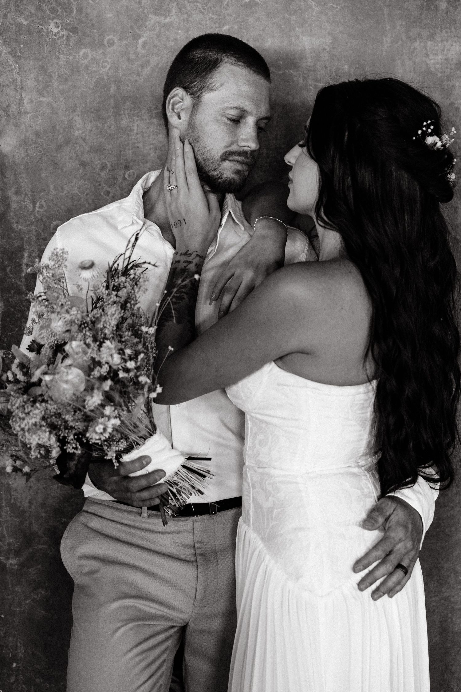 Black and white intimate portrait with dried flower bouquet against textured wall.
