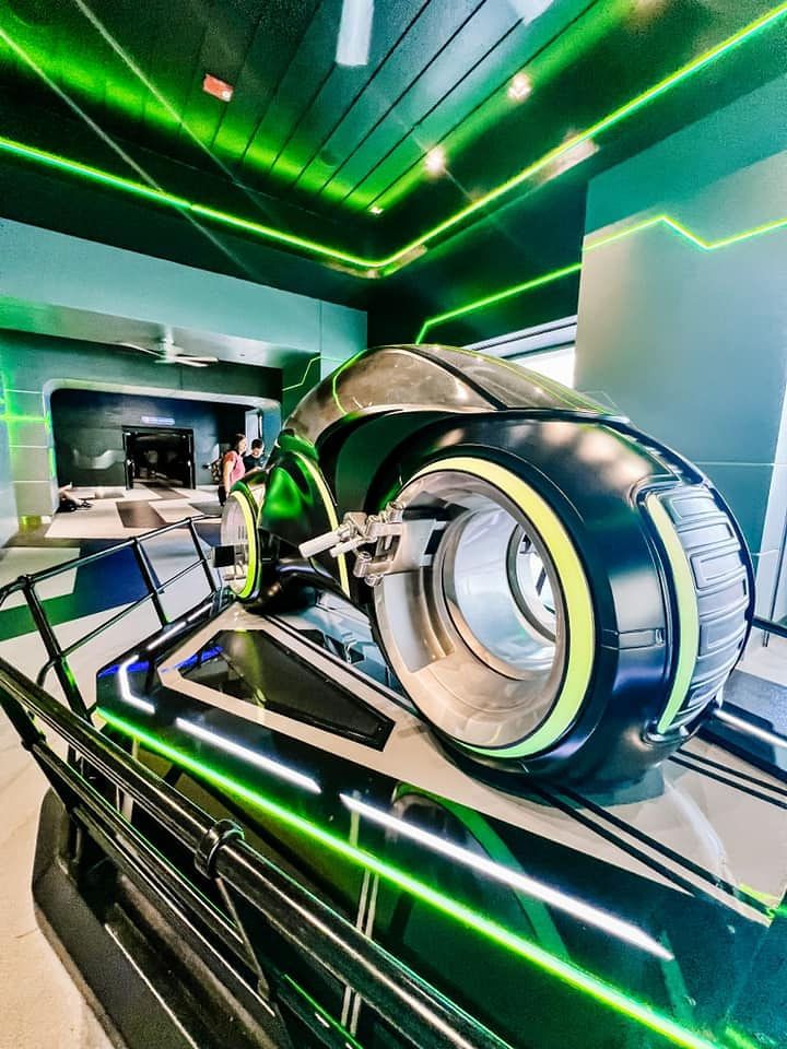 Futuristic room interior with green neon lighting and angled geometric lines featuring reflective metal surfaces.